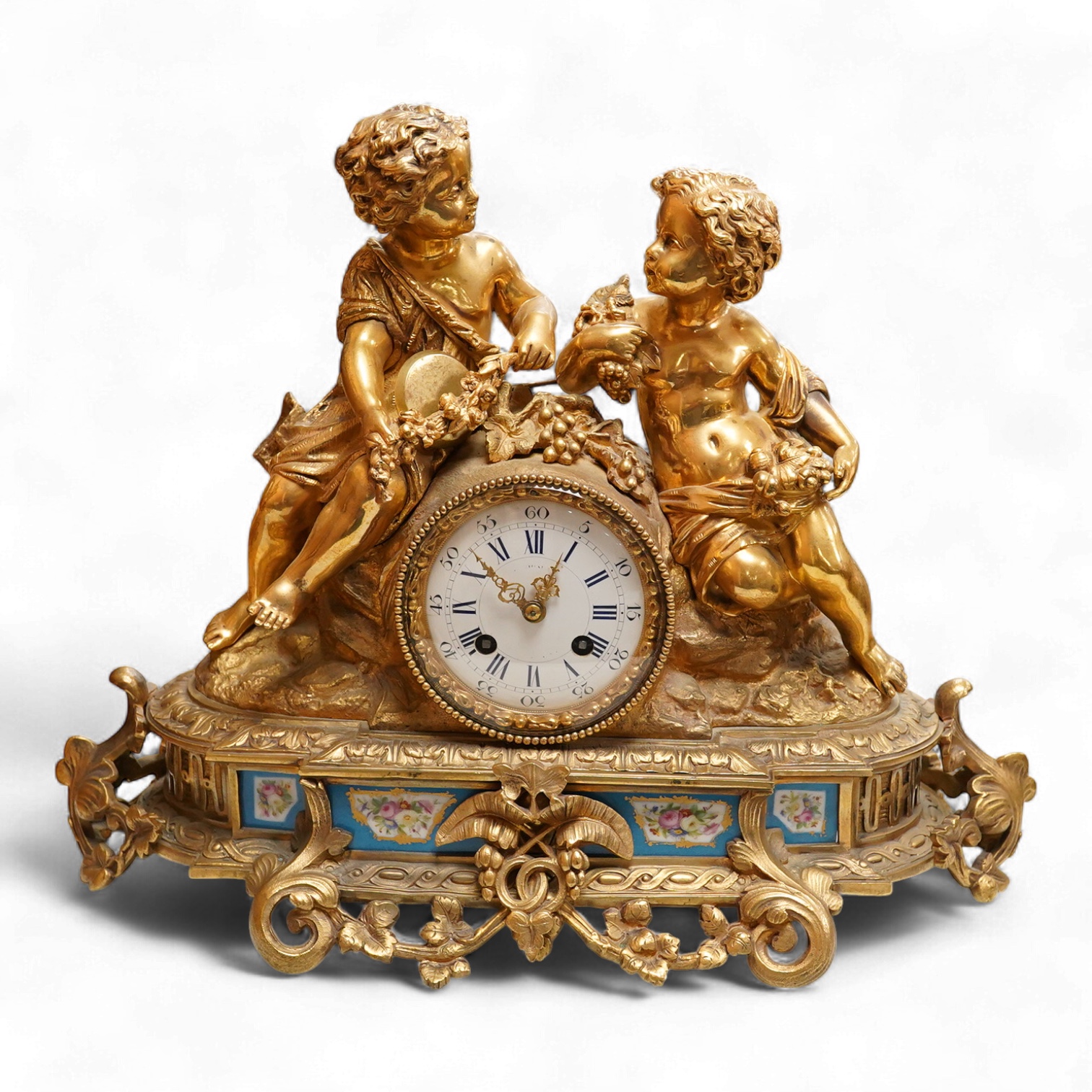 A Louis XV style figural brass mantel clock striking on a bell, with enamel dial and inset plaques, surmounted with two figures, with pendulum, no key, 42cm wide